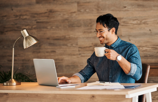 Advantages of working at Voltaira – Flexibility Smiling employee at a desk with a laptop and a coffee